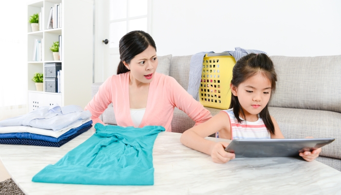 Young beautiful mother finding little girl using mobile pad computer feeling angry when she doing housework in living room.