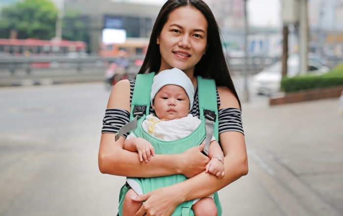 Asian mother carrying her infant baby by hipseat outdoor.