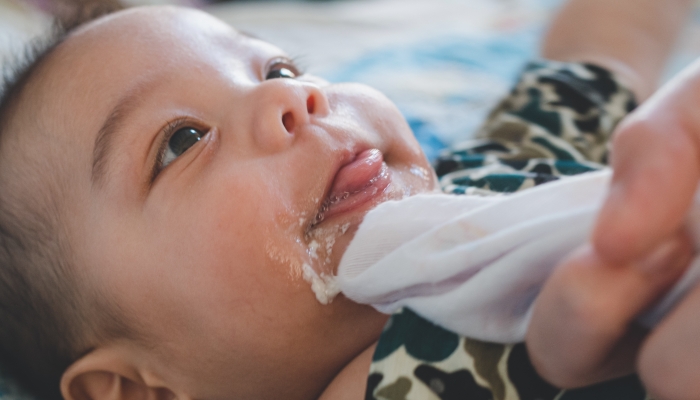 Asian mother is wiping her baby's face after infant baby boy vomiting.