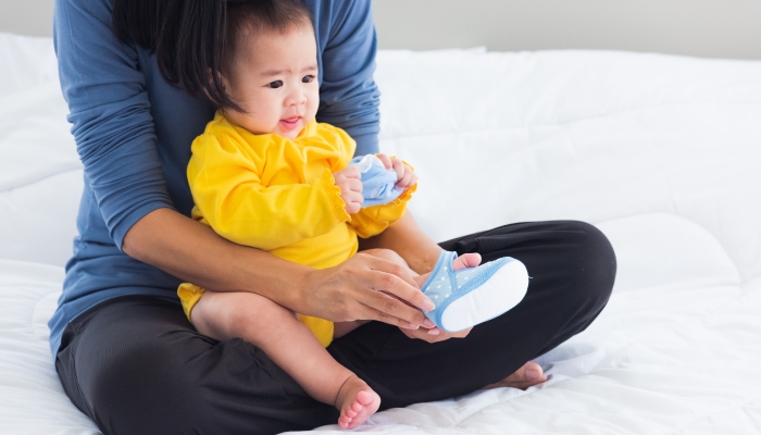 Asian young mother sitting on the bed wearing shoes to his cute baby.