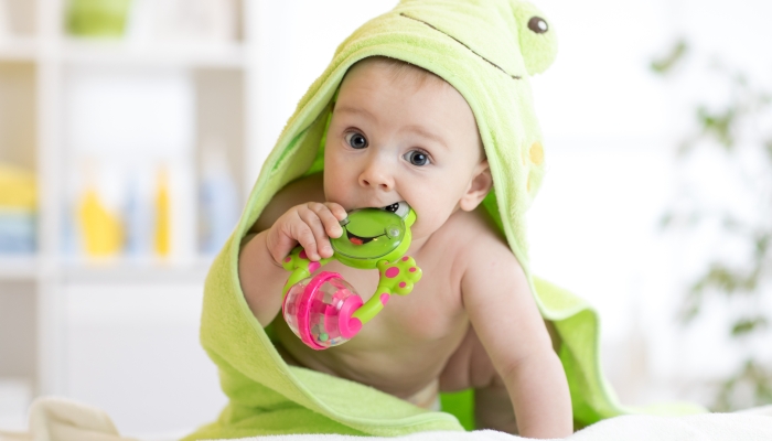 Baby boy with green towel after the bath biting toy.