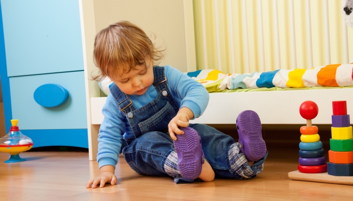 Baby learning putting on sandal sitting in the bedroom.