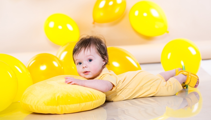 Baby lying on the cushion with yellow balloons.
