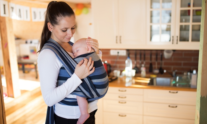 Beautiful mother in kitchen with her son sleeping in sling.