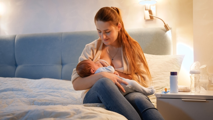 Beautiful smiling mother looking and rocking her newborn baby child eating milk and sucking breast.