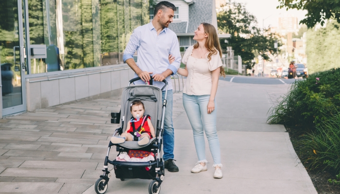 Caucasian mother and father walking with baby daughter in stroller.