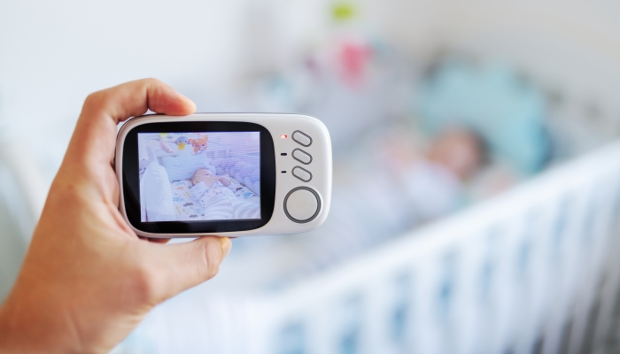 Close up of hand holding baby now modern baby monitor and recording baby in crib.