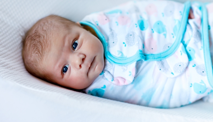 Cute adorable newborn baby wrapped in colorful blanket, looking at the camera.