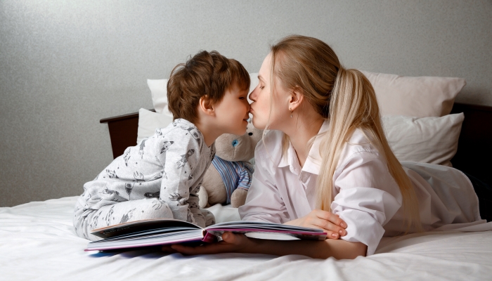 Cute preschool child son holding a book reading fairy tales for mom.