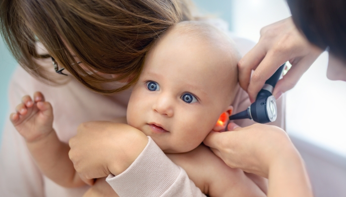 Doctor pediatrist examining childs ear with otoscope.