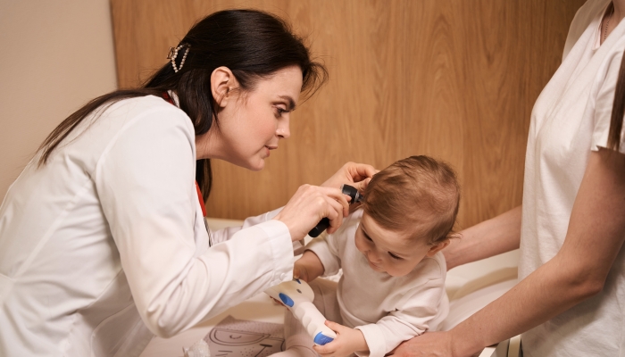 Experienced otolaryngologist examining eardrum of little baby.