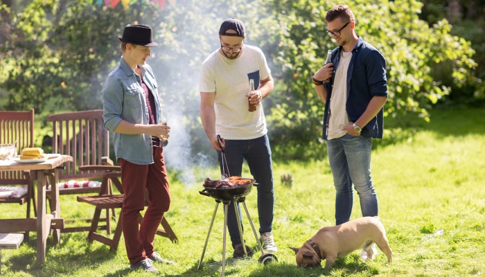 Happy friends cooking meat on barbecue grill.