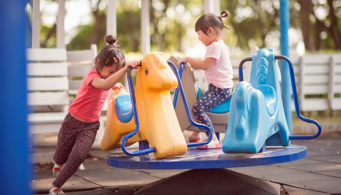 Happy funny two little children playing with merry go around at the playground.