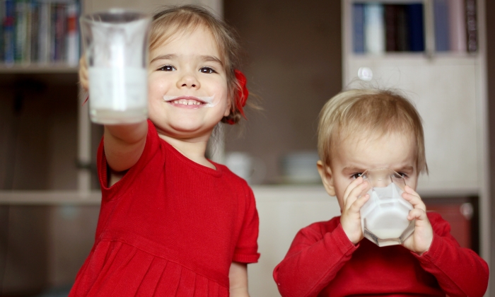 Happy gorgeous little girl with milk mustache showing an empty glass.