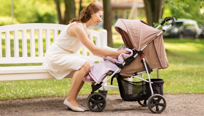 Happy mother with child in stroller at summer park.