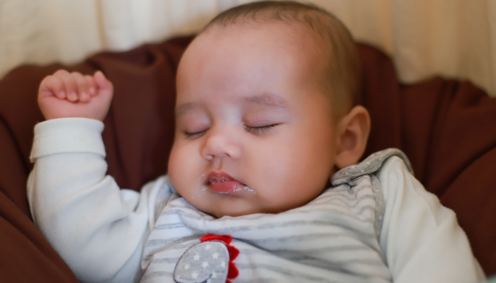 Infant newborn sleeping in bed with dirty mouth vomiting.