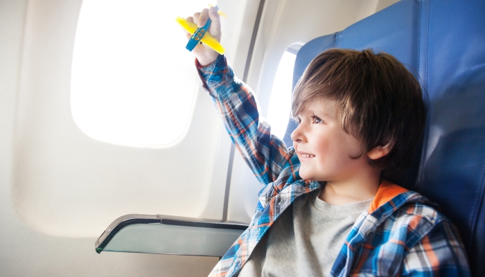 Little boy play with toy plane in the commercial jet airplane flying on vacation.