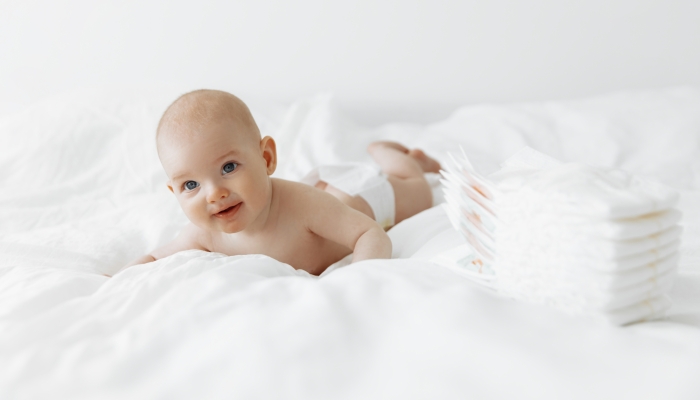 Little cute newborn baby in diapers on a white bed in the bedroom.