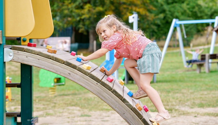 Little girl climbing on playground on summer day.