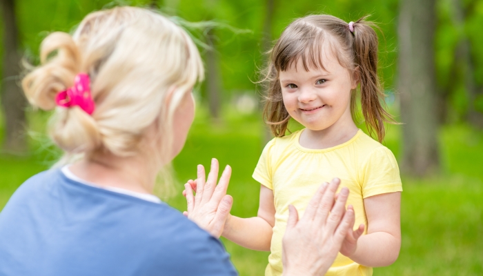 Little girl with syndrome down talks with her mother in a summer park.