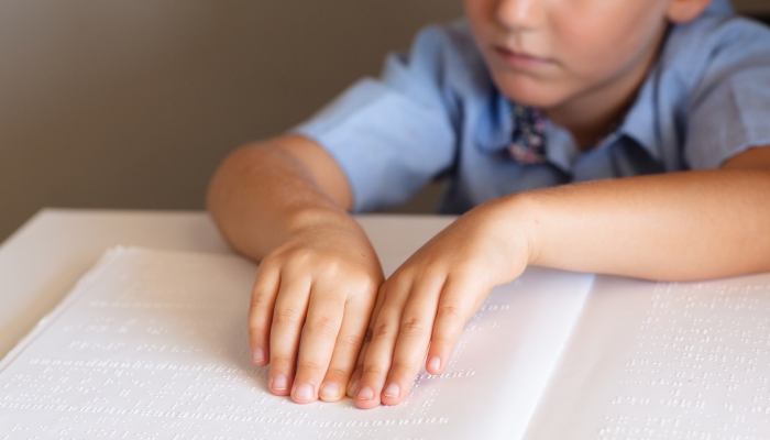 Midsection of elementary schoolboy with hands on braille at desk in classroom.