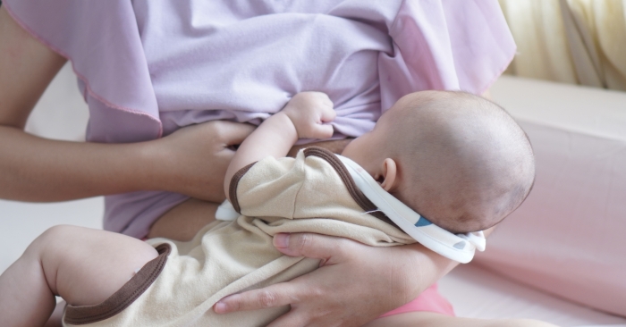 Mother breastfeeding newborn girl on bed.