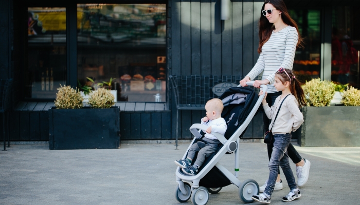 Mother walking with a baby and a stroller in the city street.