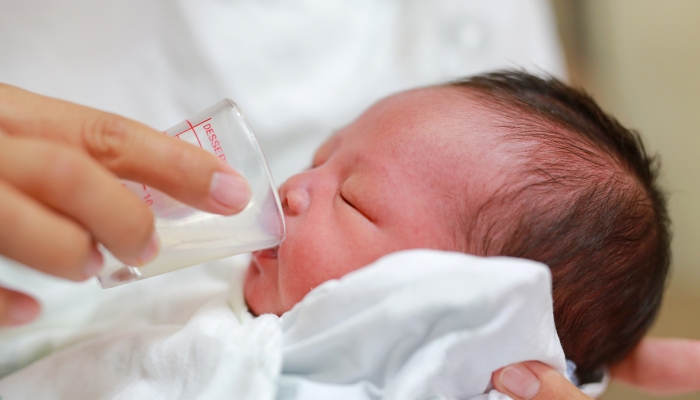 Newborn Baby drinking milk from glass cup.