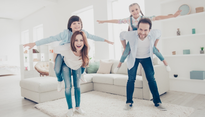Portrait of cheerful positive parents playing with kids in modern white apartments.