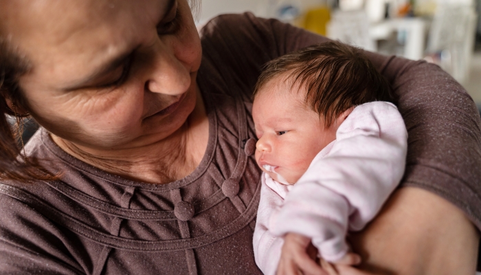 Senior caucasian woman grandmother hold newborn infant girl vomiting milk.