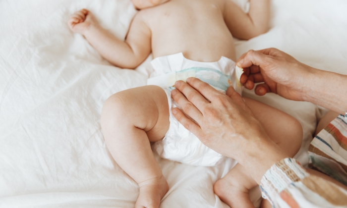 Side view portrait of a mother changing her baby's diaper on the bed, one year old baby concept.