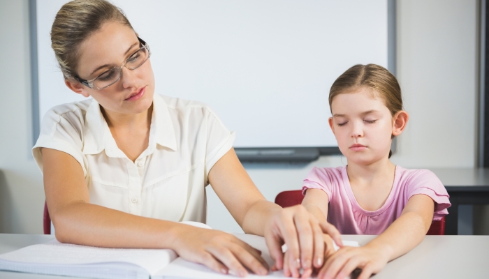 Teacher assisting blind student in library at school.