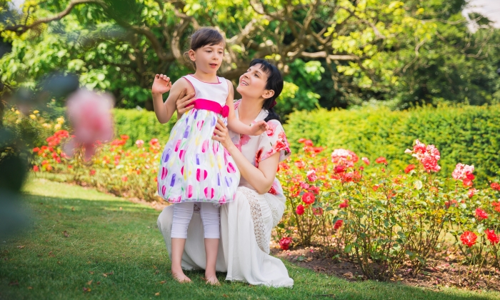 The young happy mother sitting in the garden and holding her beautiful daughter and looking at hers.