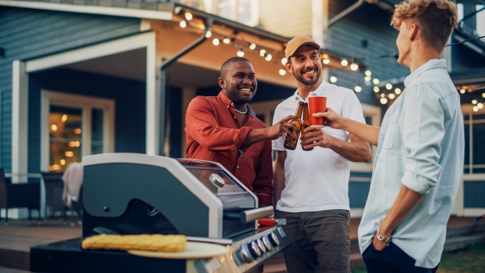 Three Happy Young Adult Men Gathered Around a Fire Grill.