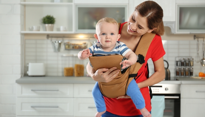 Woman with her son in baby carrier at home.