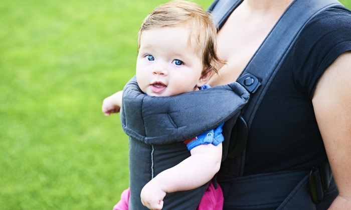 Young mother with her little baby child girl in a carrier outside in nature.