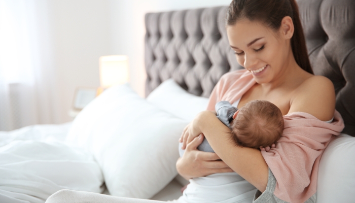 Young woman breastfeeding her baby in bedroom.