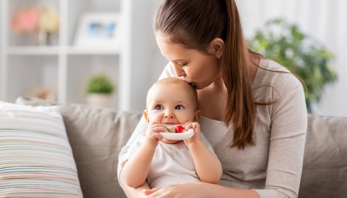 happy smiling mother kissing little baby playing with teething toy or rattle at home.