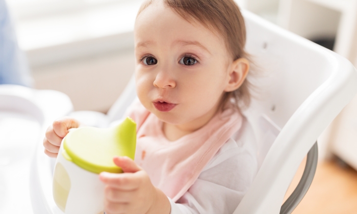 Little baby drinking from spout cup sitting in highchair at home.