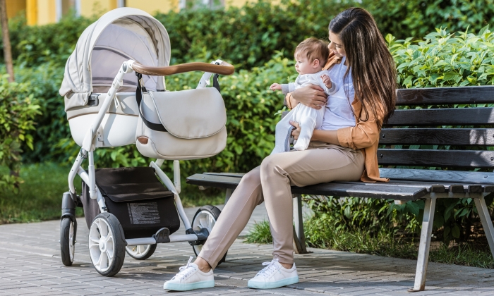 mother sitting with baby on bench near stroller in park.