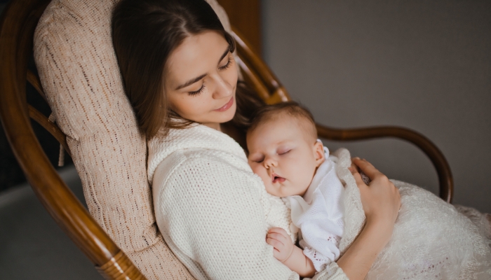 young mother holding her newborn baby sitting in armchair.