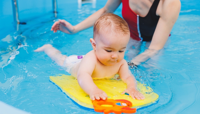 A beautiful mother teaches teaches her little son how to swim in the pool.