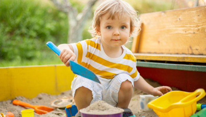 A little boy playing in the sandbox at the playground outdoors.