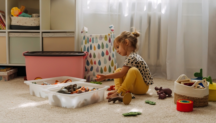 A little girl playing with toy animals and wooden blocks in nursery.