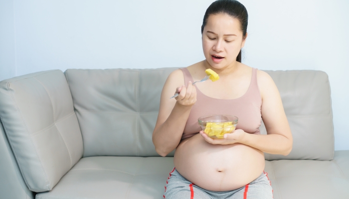 A portrait Pregnant woman sitting on couch and holding a pineapple.