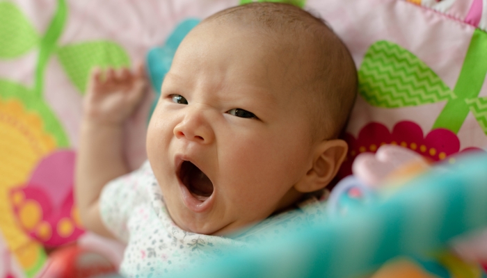 A sleepy baby yawning laying down.