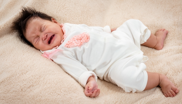 Adorable Asian newborn, dressed in white, cries with sleepiness and sleepy in a soft bed in.