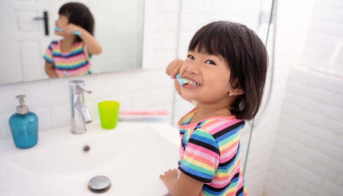 Asian little girl brushes her teeth alone in the bathroom.