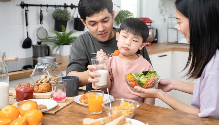 Asian parent eating breakfast with little son in the kitchen.