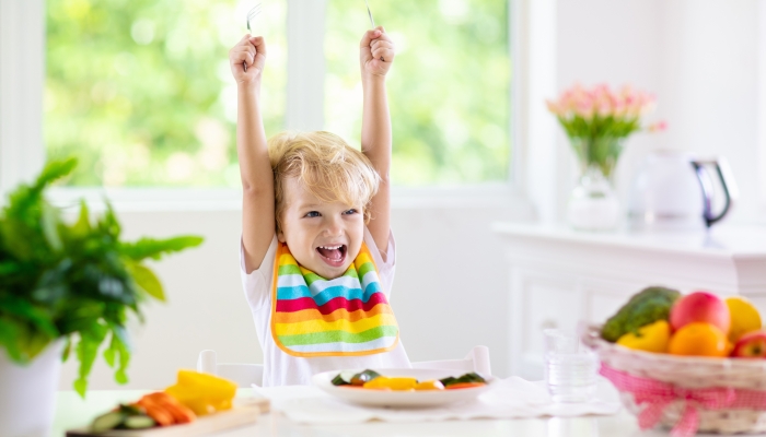 Child eating vegetables sitting in white high chair.